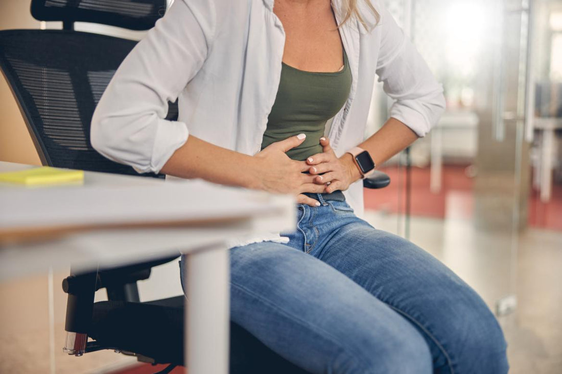 Woman sitting at a desk in an office holding her stomach as if in pain.