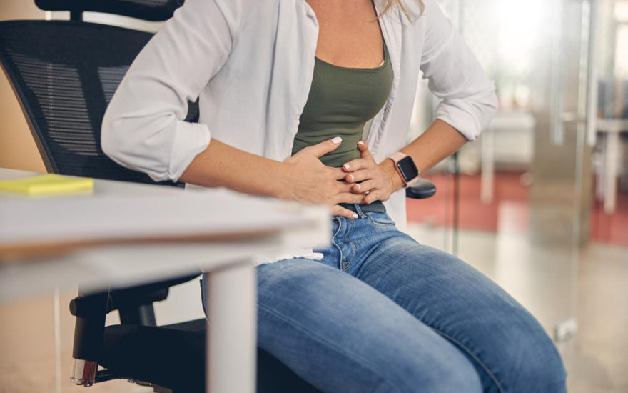 Woman sitting at a desk in an office holding her stomach as if in pain.