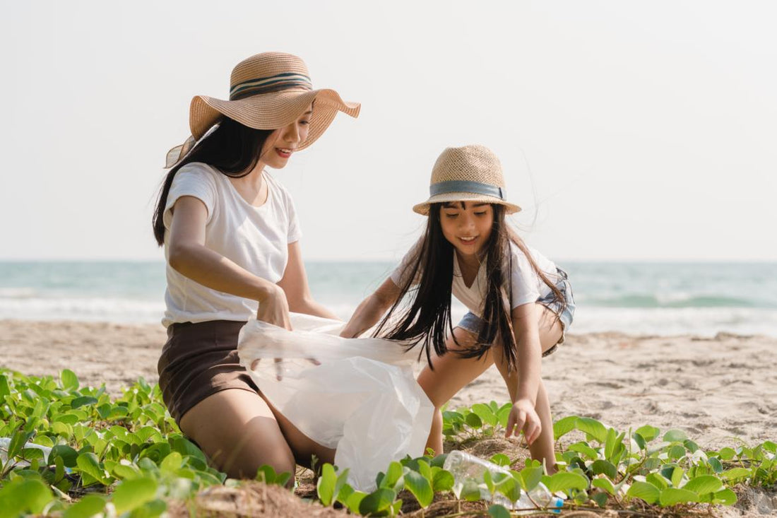 Mother and daughter duo wearing sun hats and picking up trash on the beach.