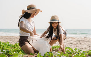 Mother and daughter duo wearing sun hats and picking up trash on the beach.