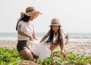 Mother and daughter duo wearing sun hats and picking up trash on the beach.