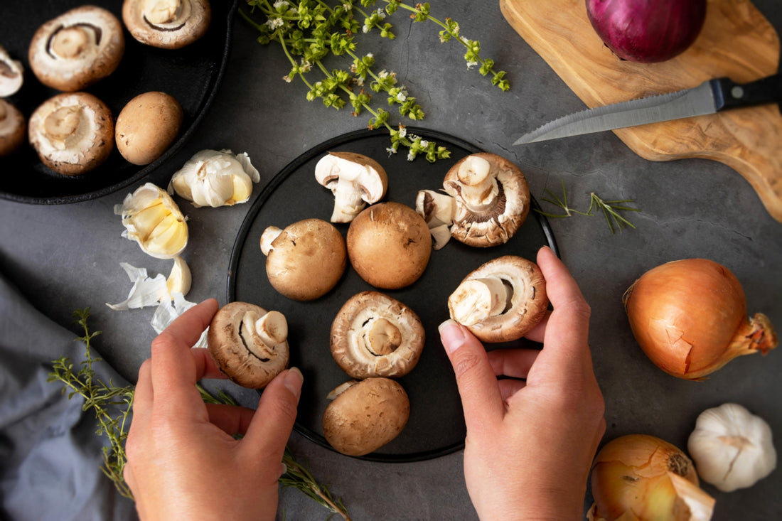 Top-down view of a pair of hands organizing fresh mushrooms on a black platter.
