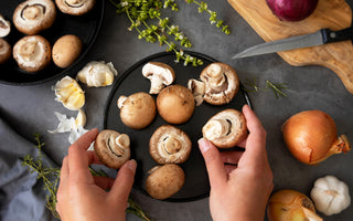 Top-down view of a pair of hands organizing fresh mushrooms on a black platter.