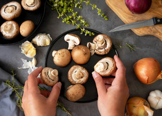 Top-down view of a pair of hands organizing fresh mushrooms on a black platter.