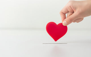 Hand holding a red heart above a slot in a white box.