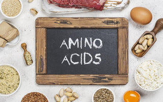 Chalkboard with amino acids written on it laying on a table with protein-rich foods surrounding it.