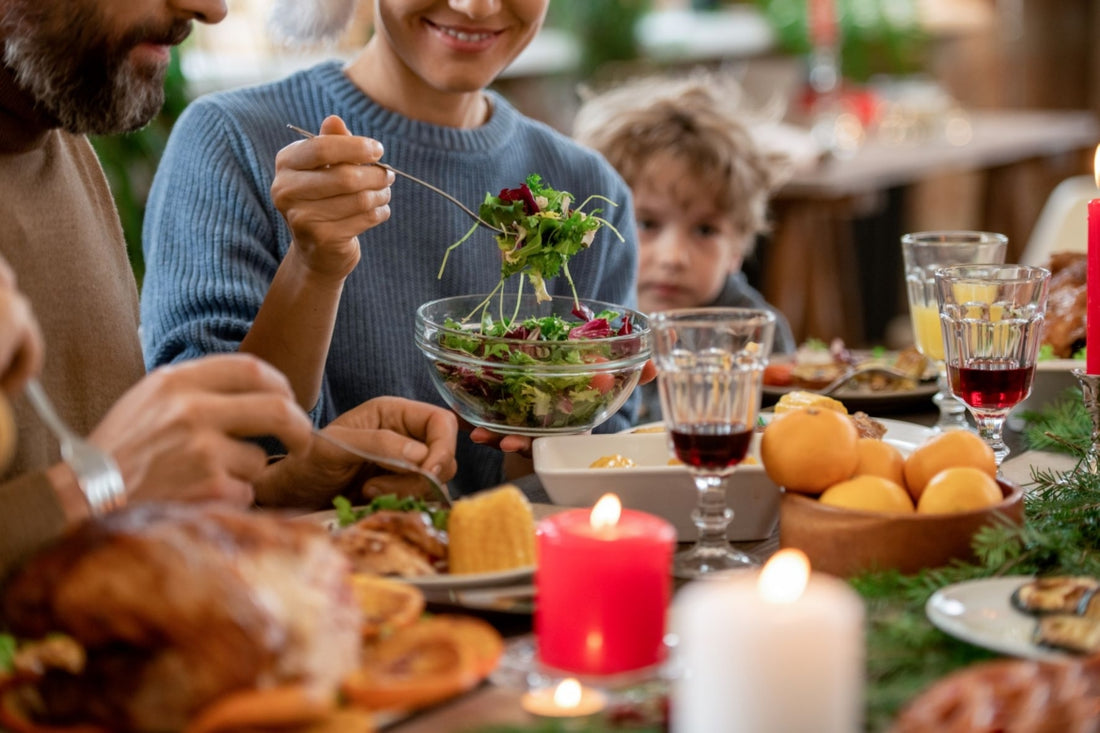 Woman in a blue sweater sitting next to a man and child at the dinner table while serving herself salad out of a glass bowl.