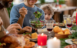 Woman in a blue sweater sitting next to a man and child at the dinner table while serving herself salad out of a glass bowl.