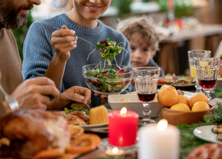 Woman in a blue sweater sitting next to a man and child at the dinner table while serving herself salad out of a glass bowl.