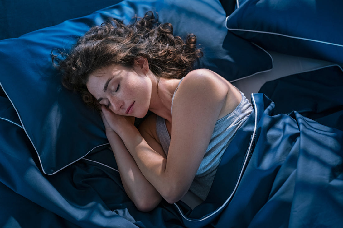 Woman sleeping on her side with dark blue bedding with her hands tucked under her head.