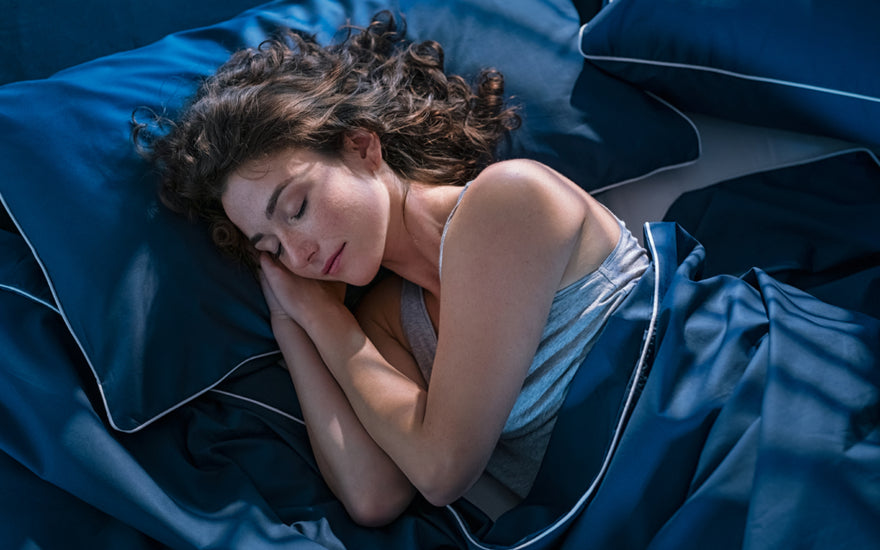 Woman sleeping on her side with dark blue bedding with her hands tucked under her head.