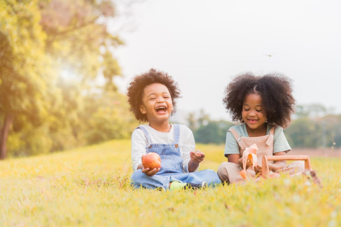 Two young children sitting in the grass while snacking on fruit. 