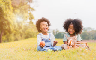 Two young children sitting in the grass while snacking on fruit. 