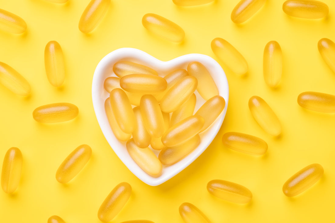 A white heart-shaped bowel filled with fish oil supplements sitting on a yellow background. 