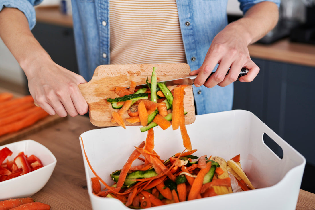 Person scraping food scraps off of a wooden cutting board and into a bin for gathering compost.