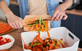 Person scraping food scraps off of a wooden cutting board and into a bin for gathering compost.