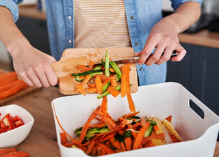 Person scraping food scraps off of a wooden cutting board and into a bin for gathering compost.