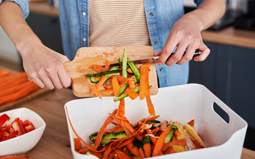 Person scraping food scraps off of a wooden cutting board and into a bin for gathering compost.