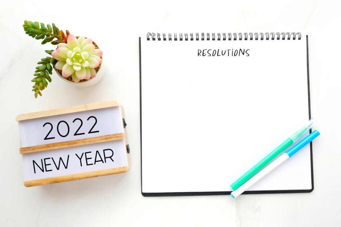 Open notebook with blank page for resolutions sitting on a table next to a sign welcoming the new year.