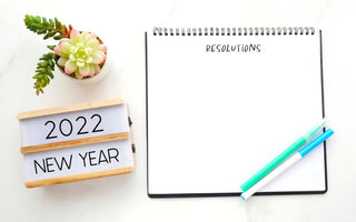 Open notebook with blank page for resolutions sitting on a table next to a sign welcoming the new year.