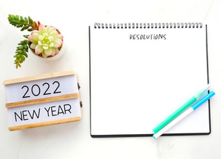 Open notebook with blank page for resolutions sitting on a table next to a sign welcoming the new year.