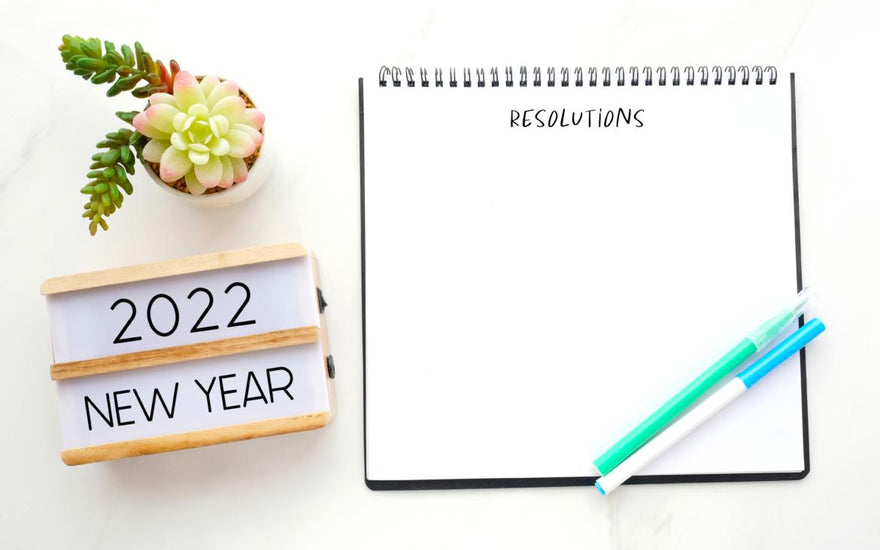 Open notebook with blank page for resolutions sitting on a table next to a sign welcoming the new year.
