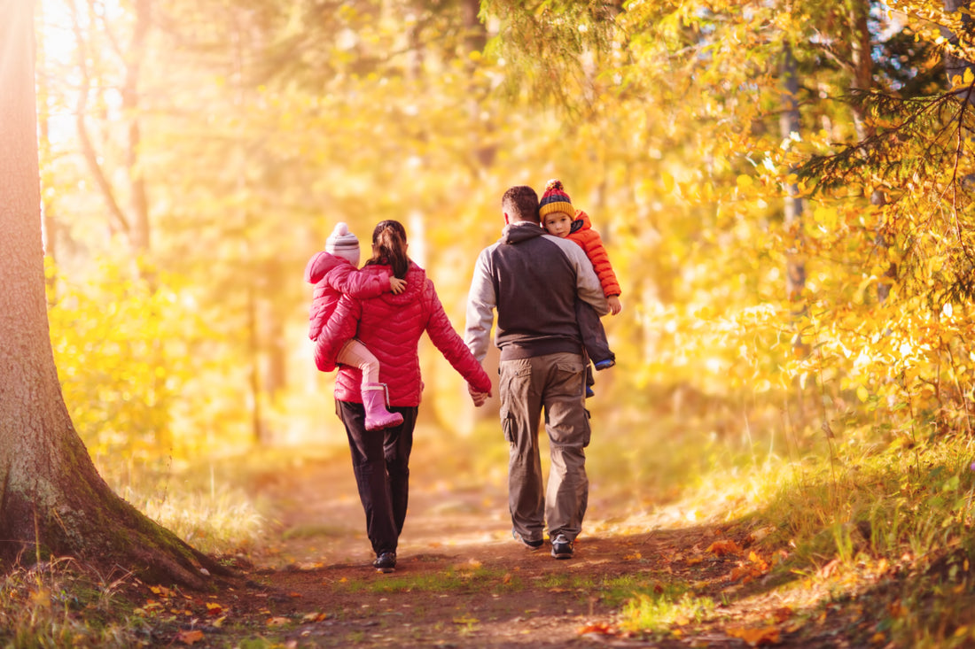 A couple holding hands while each carrying a child as they walk down a path by autumn trees.