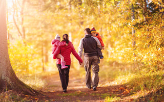 A couple holding hands while each carrying a child as they walk down a path by autumn trees.