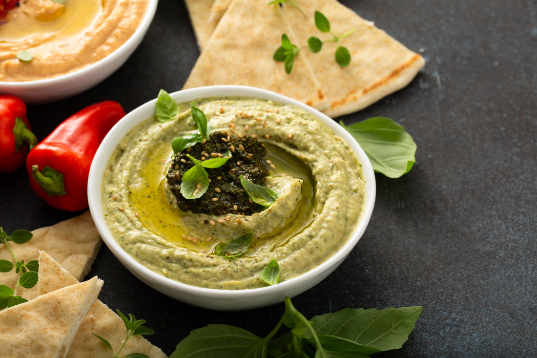 A white bowl full of green dip sitting on a black tabletop next to slices of pita bread.