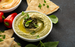 A white bowl full of green dip sitting on a black tabletop next to slices of pita bread.