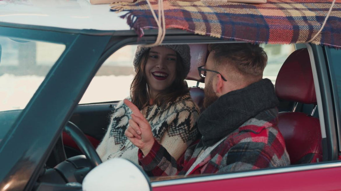 Couple dressed in winter gear sitting in a red car having a conversation.