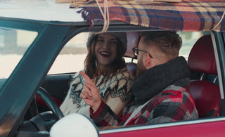 Couple dressed in winter gear sitting in a red car having a conversation.