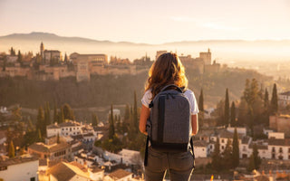 Woman wearing a gray backpack standing on a hill looking out over a city. 