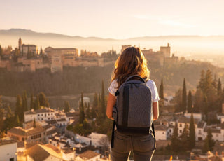 Woman wearing a gray backpack standing on a hill looking out over a city. 