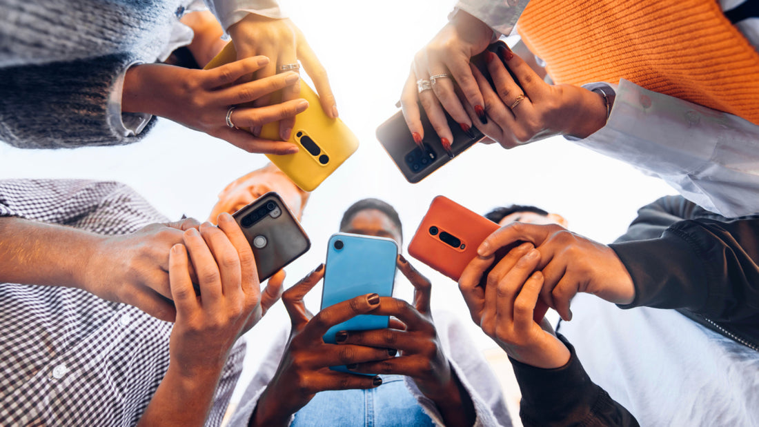 Five people standing in a circle all looking down at the cell phones in their hands.
