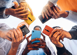 Five people standing in a circle all looking down at the cell phones in their hands.