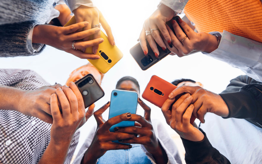 Five people standing in a circle all looking down at the cell phones in their hands.