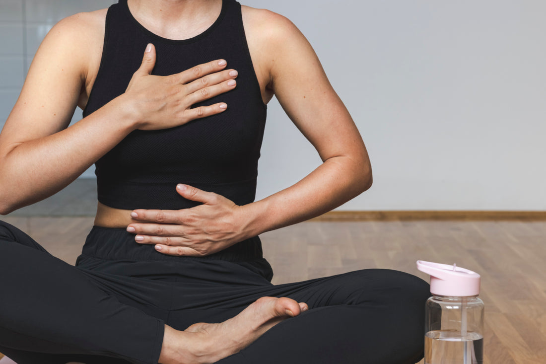 Woman in all black workout gear sitting crosslegged on the floor in a yoga pose.