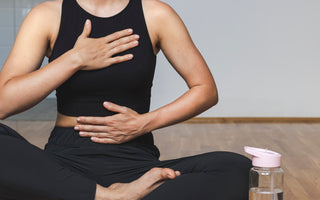 Woman in all black workout gear sitting crosslegged on the floor in a yoga pose.