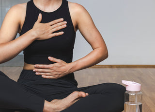 Woman in all black workout gear sitting crosslegged on the floor in a yoga pose.