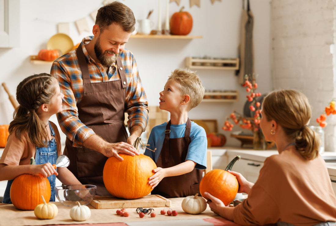 Family of four gathered around a kitchen table carving pumpkins together.