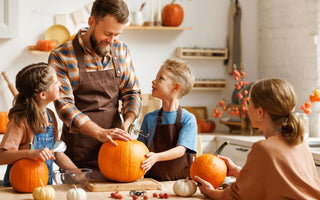 Family of four gathered around a kitchen table carving pumpkins together.