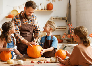 Family of four gathered around a kitchen table carving pumpkins together.