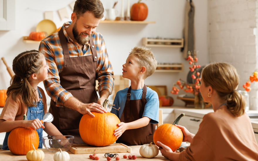Family of four gathered around a kitchen table carving pumpkins together.