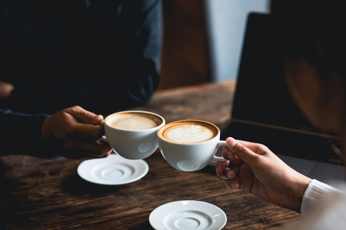 Two people clinking white coffee mugs together.