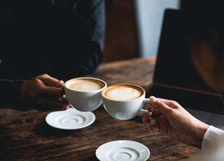 Two people clinking white coffee mugs together.