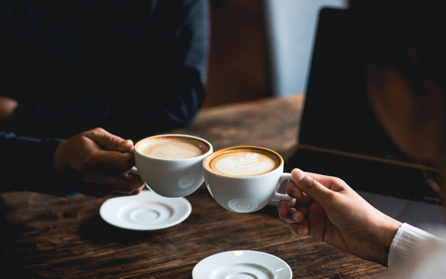 Two people clinking white coffee mugs together.