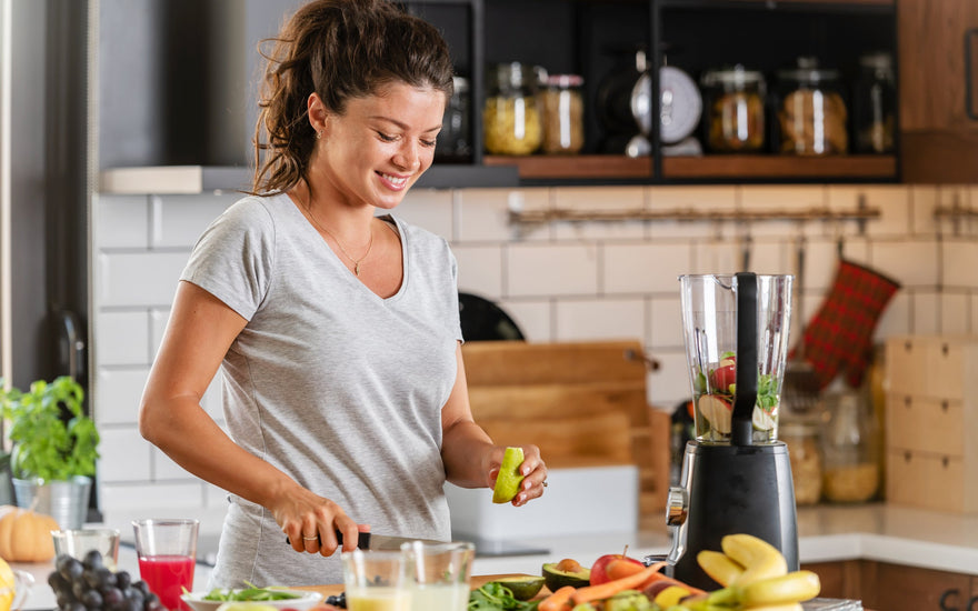 Young woman smiling in the kitchen cutting various healthy fruits to add to a blender for her smoothie.