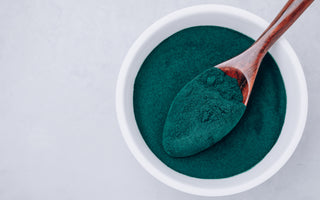 Top-down view of a white bowl and wooden spoon full of green algae powder.