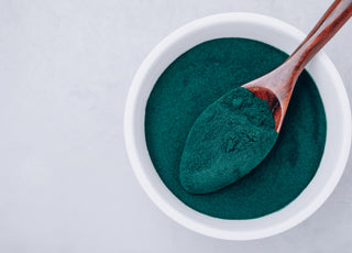 Top-down view of a white bowl and wooden spoon full of green algae powder.